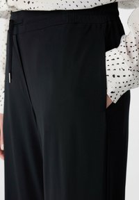 Czarne spodnie z elastyczną talią i detalem sznurków. Gładki materiał o luźnym kroju, połączony z długim topem w kropki.