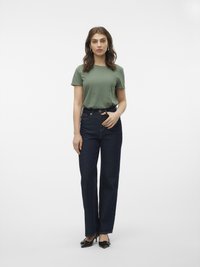 Zelena majica kratkih rukava uparena s tamnoplavim ravnim trapericama. Outfit je upotpunjen crnim cipelama na visoku petu i jednostavnim naušnicama.