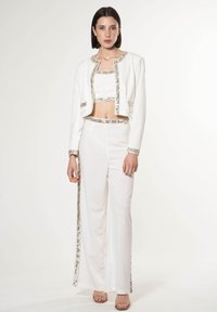 Conjunto blanco que incluye una chaqueta corta y pantalones de cintura alta. Decorado con acentos metálicos y una textura suave.