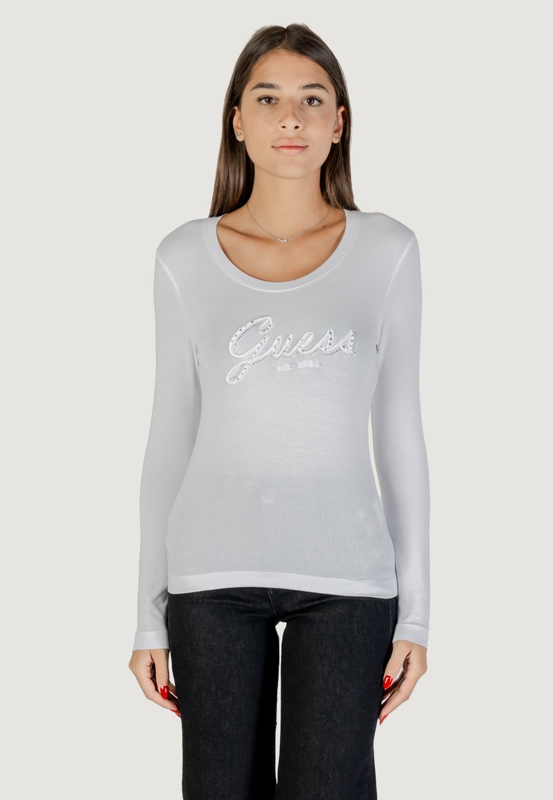 Top blanco de manga larga con escote redondo, que presenta un brillante logo de "Guess" en plata en el pecho. Tejido suave y elástico.