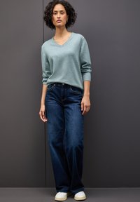 Hellblauer V-Ausschnitt-Pullover mit langen Ärmeln, kombiniert mit dunkelblauen weiten Jeans und weißen Sneakers. Strukturierter Stoff mit minimalen Details.