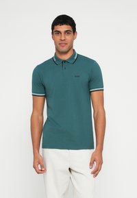 Türkizkék rövid ujjú galléros póló fekete-fehér csíkos részletekkel és egy kis fekete "BOSS" logóval a mellkasán.