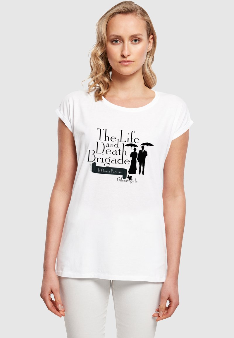 Hvit t-skjorte med korte ermer som har svart tekst og silhuetter på forsiden, med "The Life and Death Brigade" og designelementer.