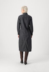 Denimová šaty košeľového strihu v tmavom praní, s vysokým golierom, dlhými rukávmi a gombíkovými manžetami, s dĺžkou po polovicu lýtok a s rovnou siluetou.