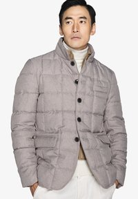 Puffjakke i lysegrå stof med en kviltet design, høj krave og sorte knapper. Indeholder sidelommer og en blød indre foring.