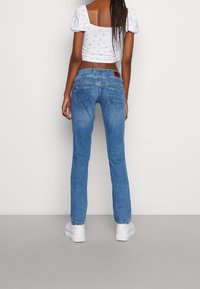 Blå denimjeans med slim fit, med bakfickor och en traditionell midja. Matchas med en vit crop top med puffärmar.