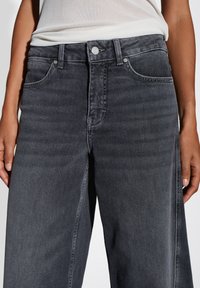 Donkergrijze denim jeans met hoge taille en rechte pijpen, voorzien van voorkruiden en een metalen knoopsluiting. Zachte textuur en minimale vervaging.