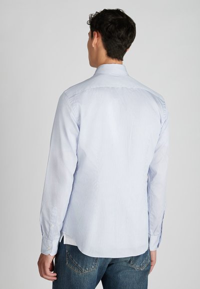 Lichtblauw langshirt met een subtiel gestreept patroon, button-down kraag en afgeronde zoom, gecombineerd met donkerblauwe jeans.