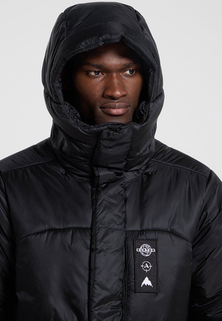 Schwarze Steppjacke mit hohem Kragen und Kapuze, mit strukturierter Oberfläche, Logopatch und durchgehendem Reißverschluss. Akzentuiert durch Ziernähten.