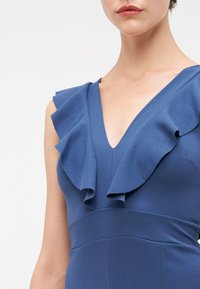 Vestido azul com um decote em V profundo e detalhes de babados assimétricos nos ombros, feito de um tecido suave com um corte estruturado.
