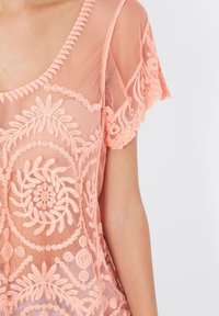 Top de malla melocotón con escote redondo y mangas cortas, que presenta patrones de bordado floral y detalles texturizados en toda su superficie.