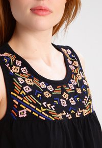 Top senza maniche nero con ricami floreali e geometrici colorati attorno al collo. Tessuto morbido con una vestibilità comoda.