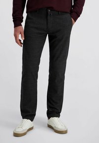 Donkergrijze geruite broek gemaakt van een gestructureerde stof, met een knoopsluiting, twee zijzakken en gecombineerd met witte sneakers.