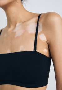 Bralette noire au design sans coutures, avec des fines bretelles réglables et une texture lisse. Présente un décolleté droit et une esthétique minimaliste.