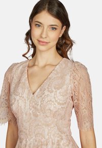 Spitzenkleid in zartem Rosa mit V-Ausschnitt und kurzen Spitzenärmeln. Mit filigranen Blumenmustern und einem taillierten Oberteil.