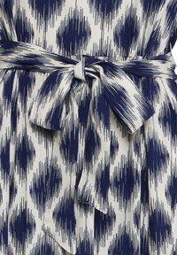 Viduklī sasieta lente uz baltas auduma ar tumši zilām nevienmērīgām vertikālām svītrām dimanta rakstā uz kleitas vai apģērba.