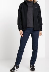 Svart lättviktsjacka med hög krage, i kombination med en mörkgrå turtleneck och marinblå byxor. Bärs med svart och vita sneakers.