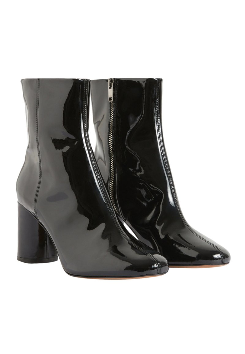 Un par de botines de charol negro brillante con tacones de bloque y cremalleras laterales sobre un fondo blanco.