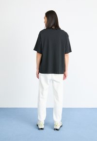 Kortermige zwarte T-shirt met een losse pasvorm, gecombineerd met witte joggers. De outfit wordt aangevuld met meerkleurige sportschoenen.