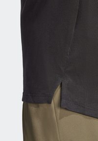 T-shirt en coton noir avec un col rond, des fentes sur les côtés et une finition texturée ; présente une étiquette rectangulaire sur l'ourlet inférieur.