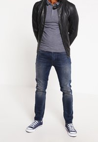 Černá kožená bunda, šedé polo tričko, modré džínové kalhoty a námořnické tenisky s bílou podrážkou. Neformální outfit s dobře padnoucím designem.