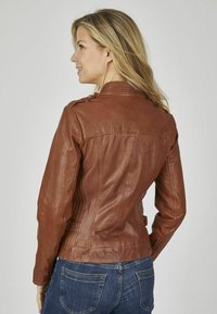 Braune Lederjacke mit figurbetontem Design, strukturierten Schulterdetails und seitlichen Schnallen. Getragen mit blauen Jeans, die die Rückansicht zeigen.