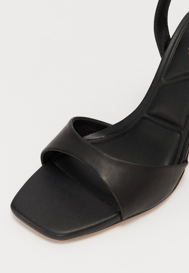 Sandale noire à talon haut avec un bout carré, une large bride sur le pied et une surface en cuir texturé avec une finition lisse.