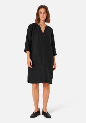 Schwarzes Leinenkleid mit V-Ausschnitt, dreiviertel Ärmeln und seitlichen Schlitzern. Das Design ist locker sitzend, glatt in der Textur und knielang.