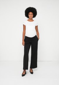 Top bianco corto con scollatura arrotondata, abbinato a pantaloni neri a gamba larga. Scarpe nere completano l'outfit. Design semplice e moderno.