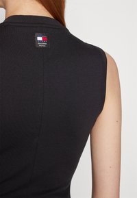 Svart ärmlös topp med ribbat mönster. Har en liten märkesetikett på baksidan nära halsringningen, som visar logotypen i vitt, rött och blått.