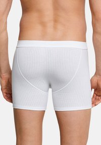 Tronchi bianchi da uomo in cotone, con una texture a coste, cinturino elastico e sottili strisce orizzontali. Vista posteriore, che mette in evidenza la vestibilità e il design.
