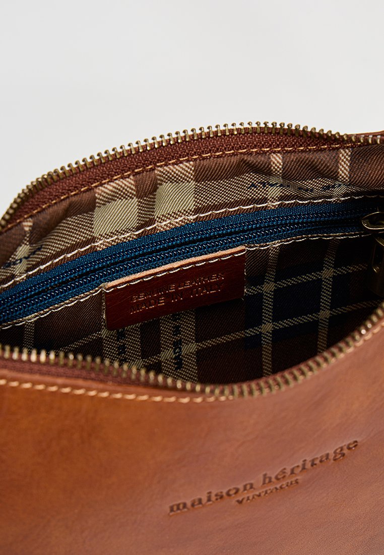 Braune Ledertasche mit einem Reißverschluss, ausgestattet mit einem karonierten Innenfutter in Beige und Blau. Ein Etikett trägt die Aufschrift "Echtes Leder, in Italien hergestellt."