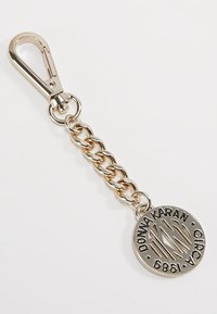 Gold-tone keychain featuring a lobster clasp and circular pendant with "DONNA KARAN CIRC 6861" engraving and cut-out design.