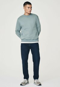 Sudadera de cuello redondo azul claro, jeans azul marino y zapatillas gris. La sudadera tiene un cuello y puños acanalados, con un corte relajado.