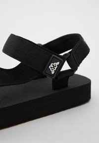Svarta sandaler med en strukturerad gummisula, utrustade med två justerbara canvasremmar och en varumärkesaccent i svart och vitt för stängning.