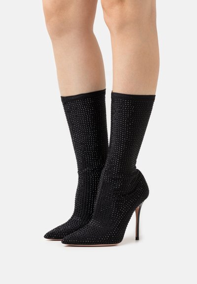 Black high-heel boots with pointed toes, textured sock-like fit, and covered in small rhinestones for added detail.