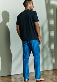 Fekete, rövid ujjú póló, amely kék csíkozott pizsamanadrággal van párosítva. Az anyag lágy érzetű, a csíkok függőlegesek és egyenletesen helyezkednek el.