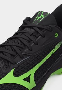 Μαύρο αθλητικό παπούτσι με υφή στην επιφάνεια, έντονα πράσινα διακοσμητικά στοιχεία και μαύρα κορδόνια σε λευκό φόντο.