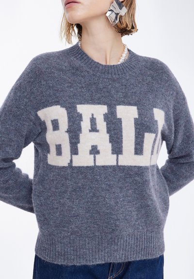 Pelēka vilnas džemperis ar krēmkrāsas "BALI" logotipu uz krūtīm, apaļu kakla izgriezumu un ribota apakšmalu. Saskaņots ar tumša denima džinsiem.