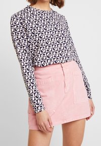 Langärmliges Oberteil in Marineblau und Creme mit geometrischem Muster, kombiniert mit einem hellrosa Jeansrock, der zwei Vorderaschen und einen Knopfverschluss hat.