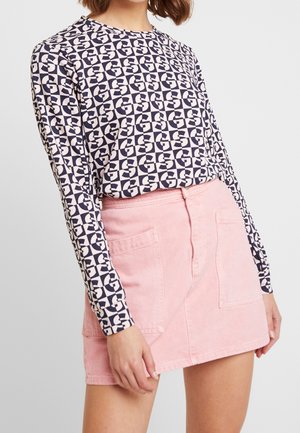 Maglietta a maniche lunghe in blu navy e crema con un motivo geometrico, abbinata a una gonna in denim rosa chiaro con due tasche frontali e chiusura con bottone.