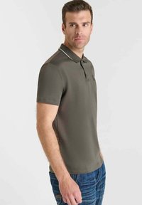 Polo de color verde oscuro con un corte ajustado, con mangas cortas y una tapeta de dos botones, realzado por un ribete blanco en el cuello.