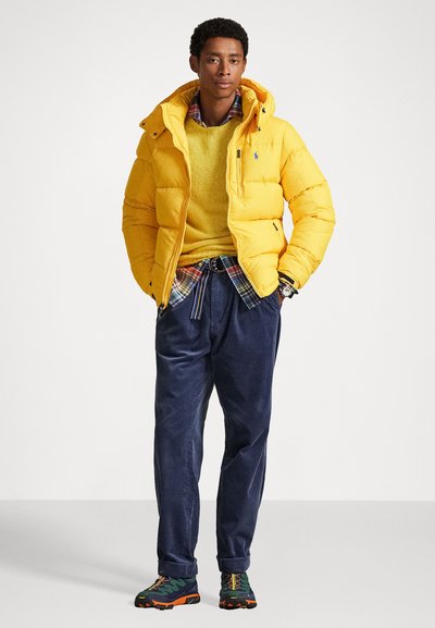 Yellow puffer jacket with a hood, a yellow knit sweater underneath, plaid shirt, navy corduroy pants, and multicolored sneakers.