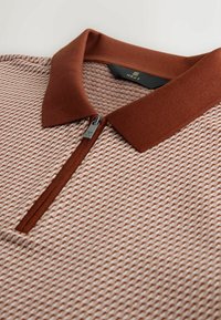 Kortärmelig poloshirt in een gestructureerde beige gebreide stof met een bruine kraag, voorzien van een ritssluiting tot een kwart van de lengte en een subtiel zigzagpatroon door het hele kledingstuk.