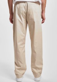 Pantaloni bej, cu croială largă, dintr-un material neted, cu un design simplu, talie elastică și buzunare laterale, asortați cu adidași albi.