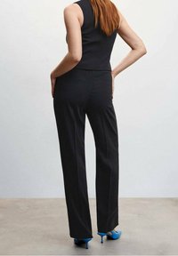 Czarne dopasowane spodnie o prostym kroju, zestawione z jasnoniebieskimi butami na wysokim obcasie. Strój uzupełnia dopasowany, bezrękawnik top.