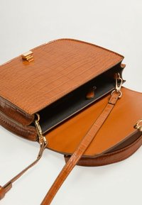 Brązowa torebka ze skóry z tłoczeniem imitującym krokodyla, z złotym zapięciem, pojedynczym paskiem na ramię oraz gładkim wnętrzem z kontrastową czarną podszewką.