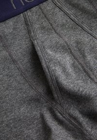 Boxer-briefs en tissu gris avec une taille bleu marine, dotés d'une texture douce, de coutures plates et d'une poche profilée pour le confort et l'ajustement.
