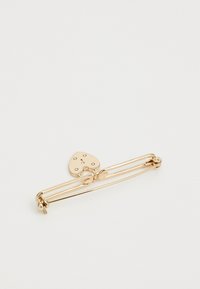 Spilla di sicurezza in tono oro con dettaglio a forma di cuore, texture liscia e due elementi decorativi aggiuntivi lungo la spilla.