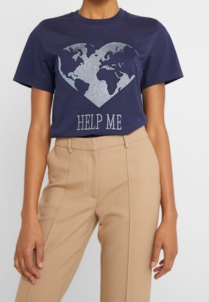 Persoon die een donkerblauw T-shirt draagt met een wereldkaart in de vorm van een hart en de tekst "HELP ME" eronder, gecombineerd met beige broek.